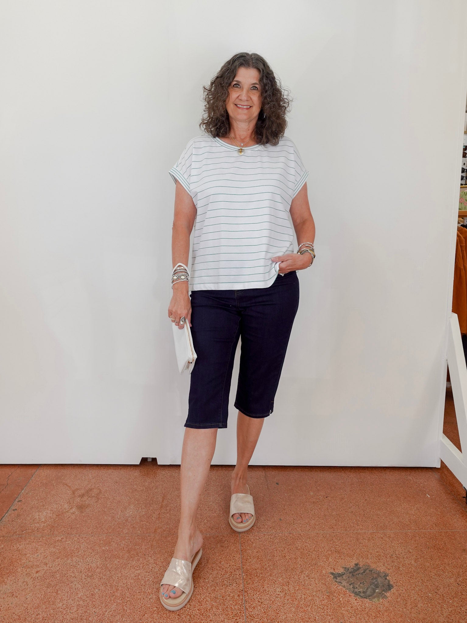 Woman wearing a striped shirt and navy shorts standing against a white wall.