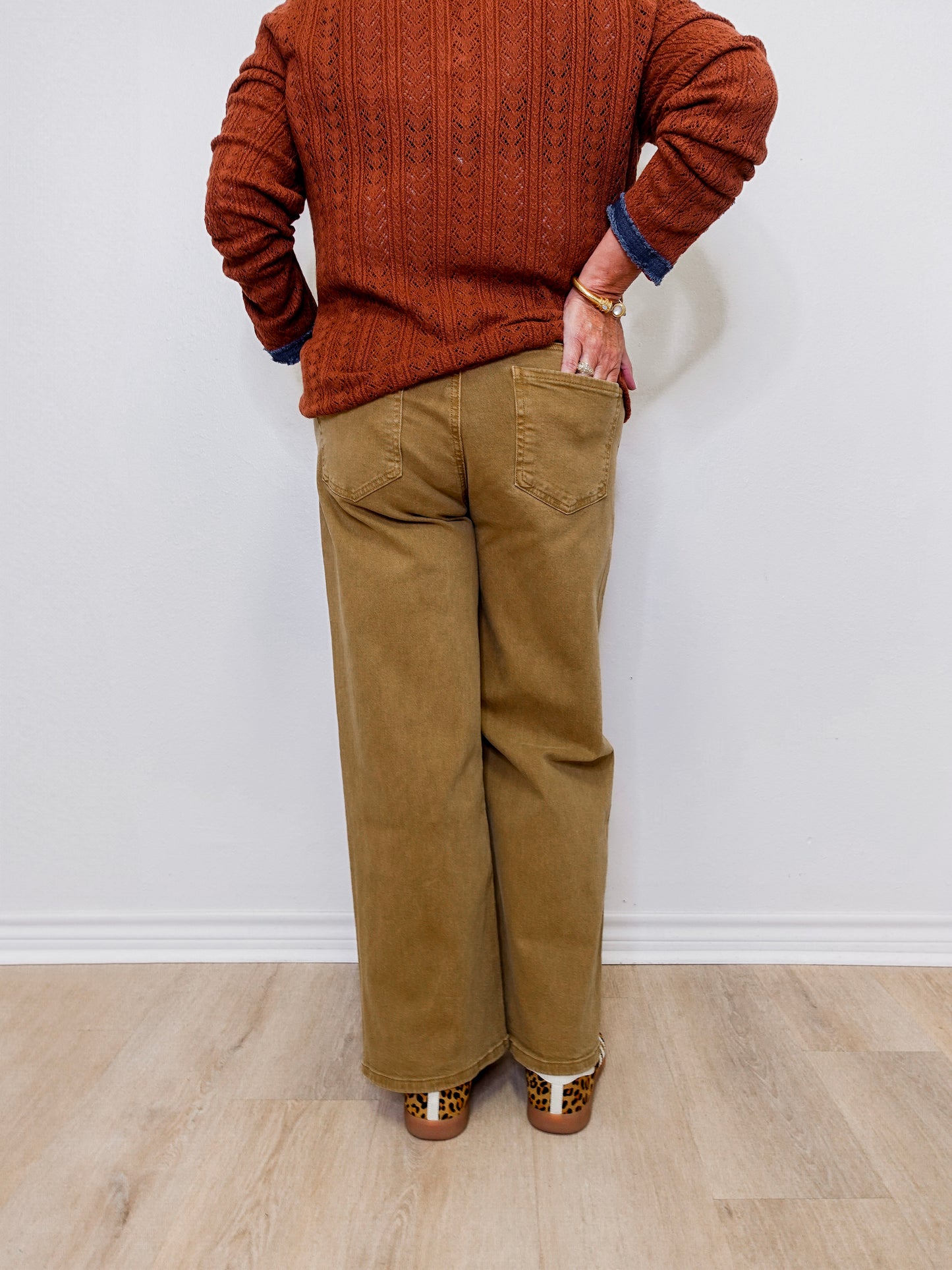 Person wearing a brown sweater and tan pants standing against a white wall.