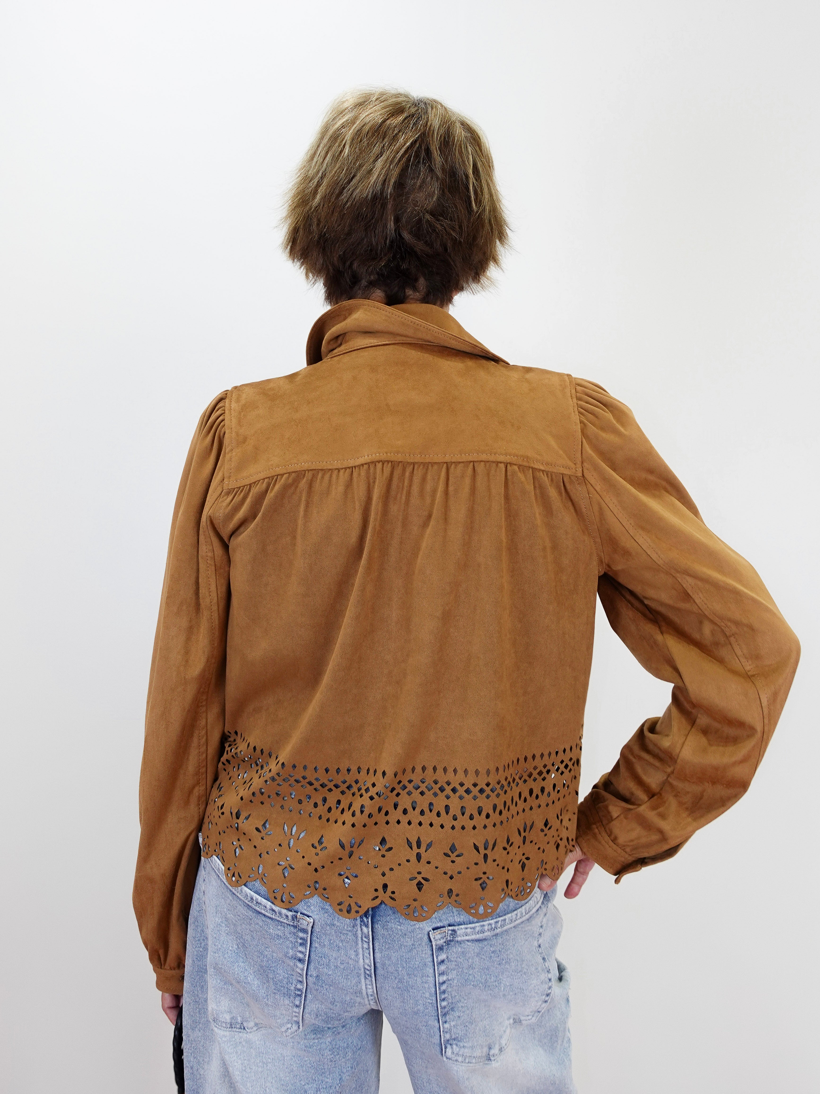 A person shown from the back wearing a brown suede-like long-sleeve blouse with a scalloped eyelet lace hem, paired with light blue jeans, against a plain light gray background.