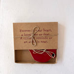 Red heart-shaped object in a brown box with a sentimental message on a white background