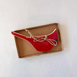 Red ceramic spoon rest in a cardboard box on a white background