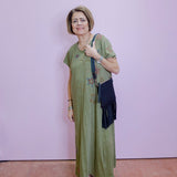 Woman in a green dress with floral patterns standing against a light purple wall.