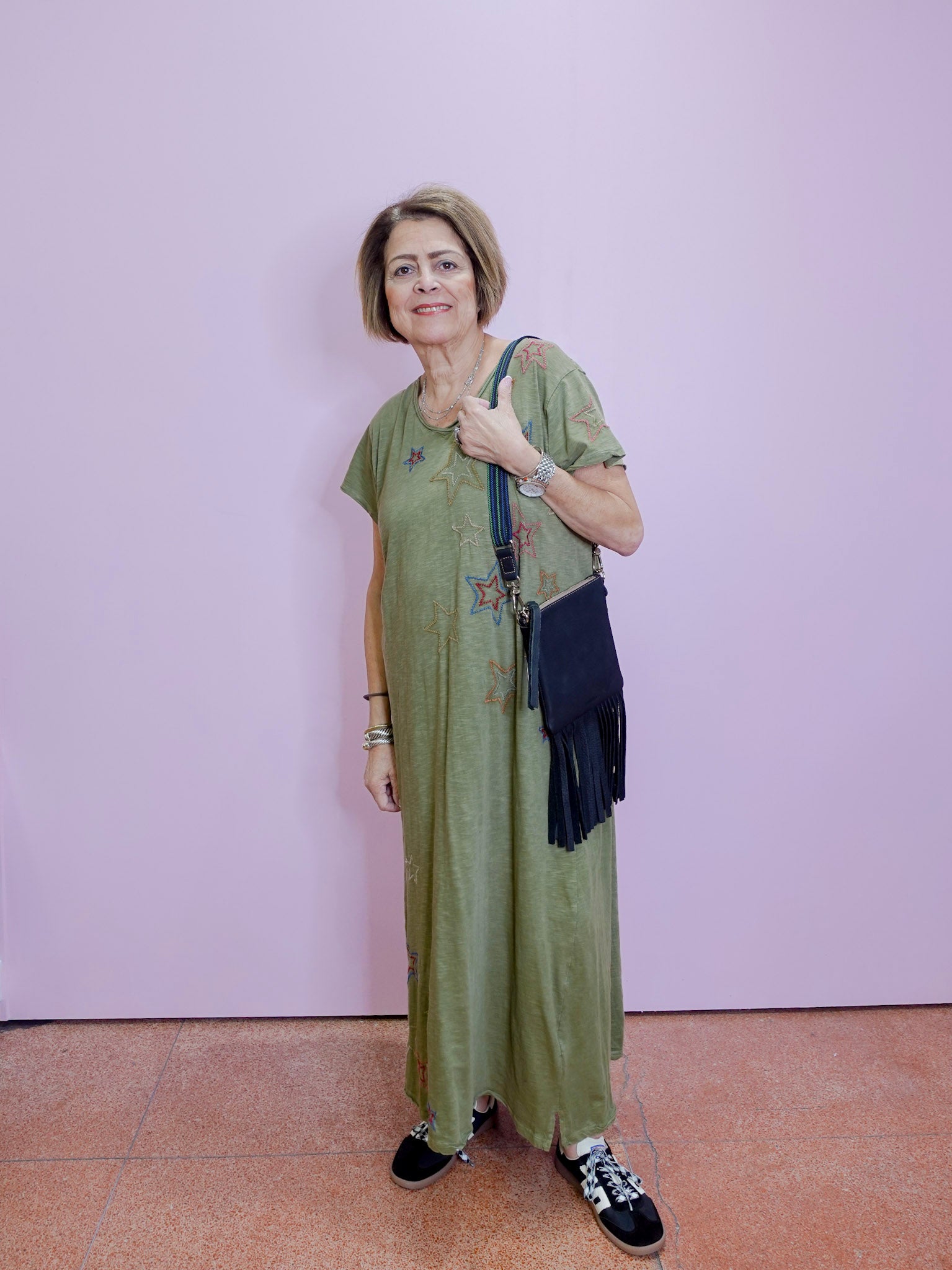 Woman in a green dress with floral patterns standing against a light purple wall.