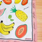Fruit-themed fabric square with bananas, pineapples, and watermelons on a wooden surface.