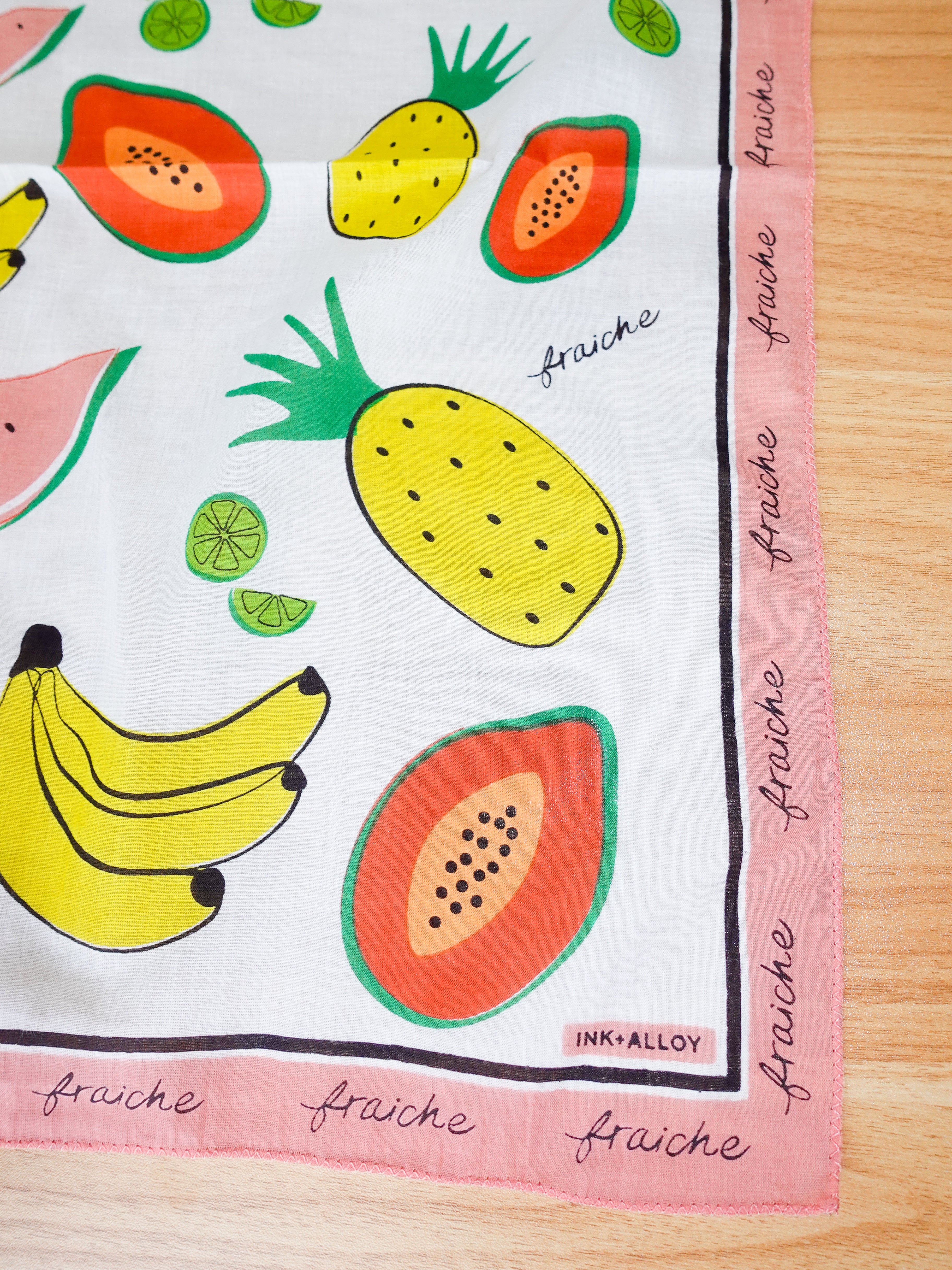 Fruit-themed fabric square with bananas, pineapples, and watermelons on a wooden surface.