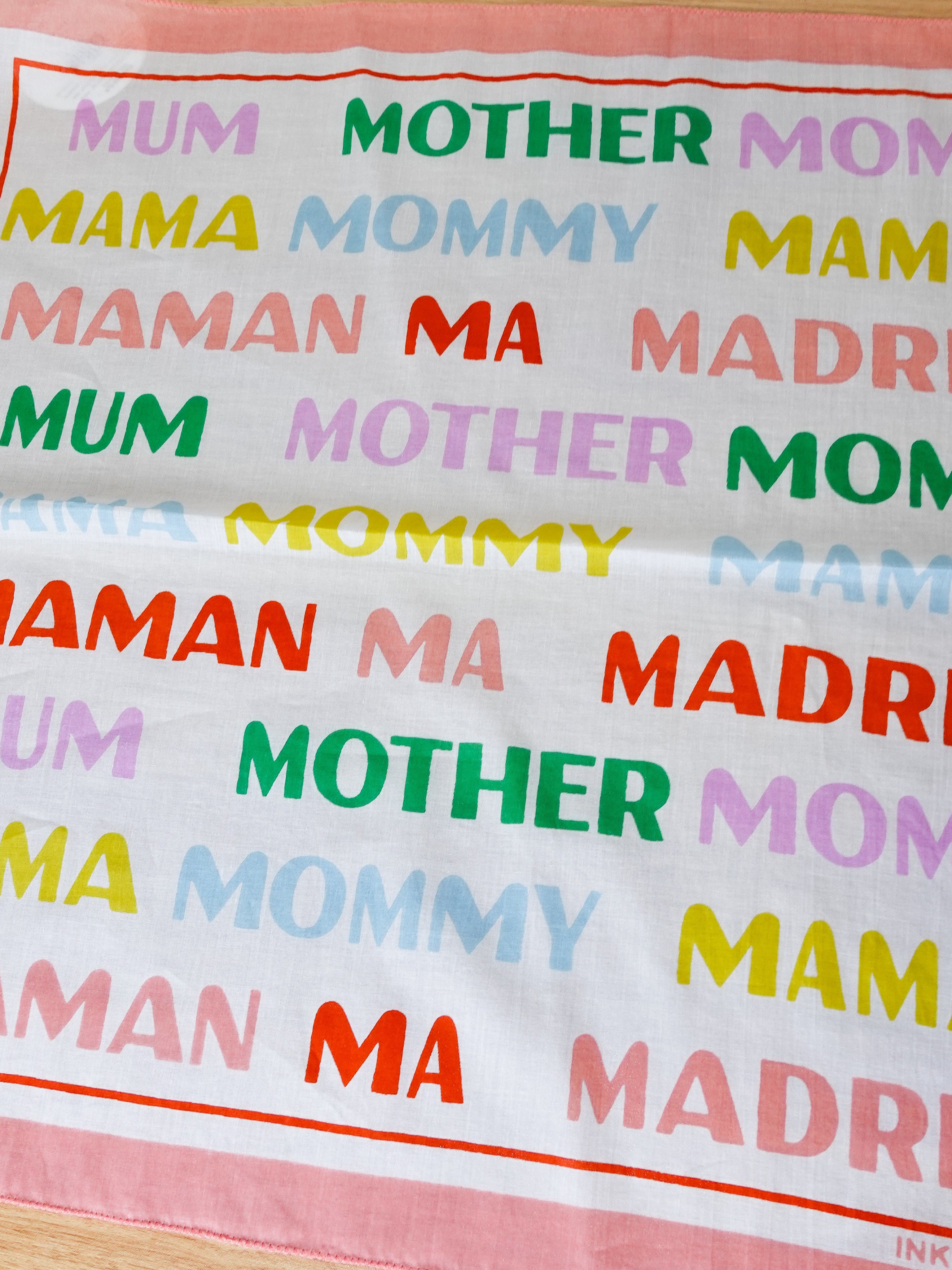 Textual fabric with 'MUM', 'MOTHER', 'MAMA', 'Mommy', 'MAMAN', 'MA', 'MADRE' in various colors on a white background.
