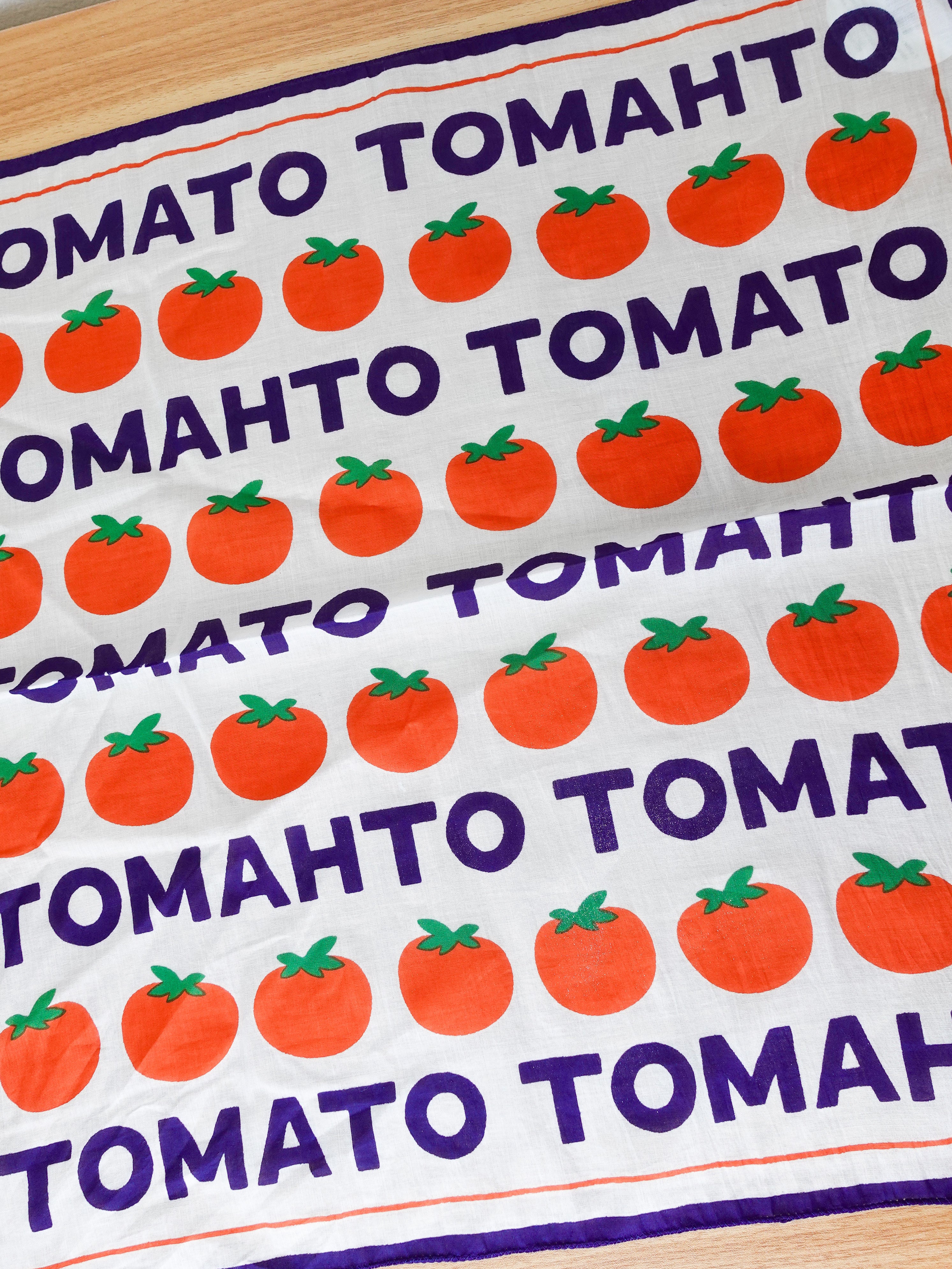 Tea towel with tomato and 'Tomato Tomato' text pattern on a wooden surface