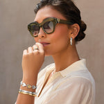Woman wearing sunglasses, a ring, and bracelets against a neutral background