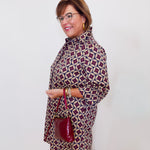 Woman wearing a patterned dress with a red handbag against a white background