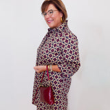 Woman wearing a patterned dress with a red handbag against a white background