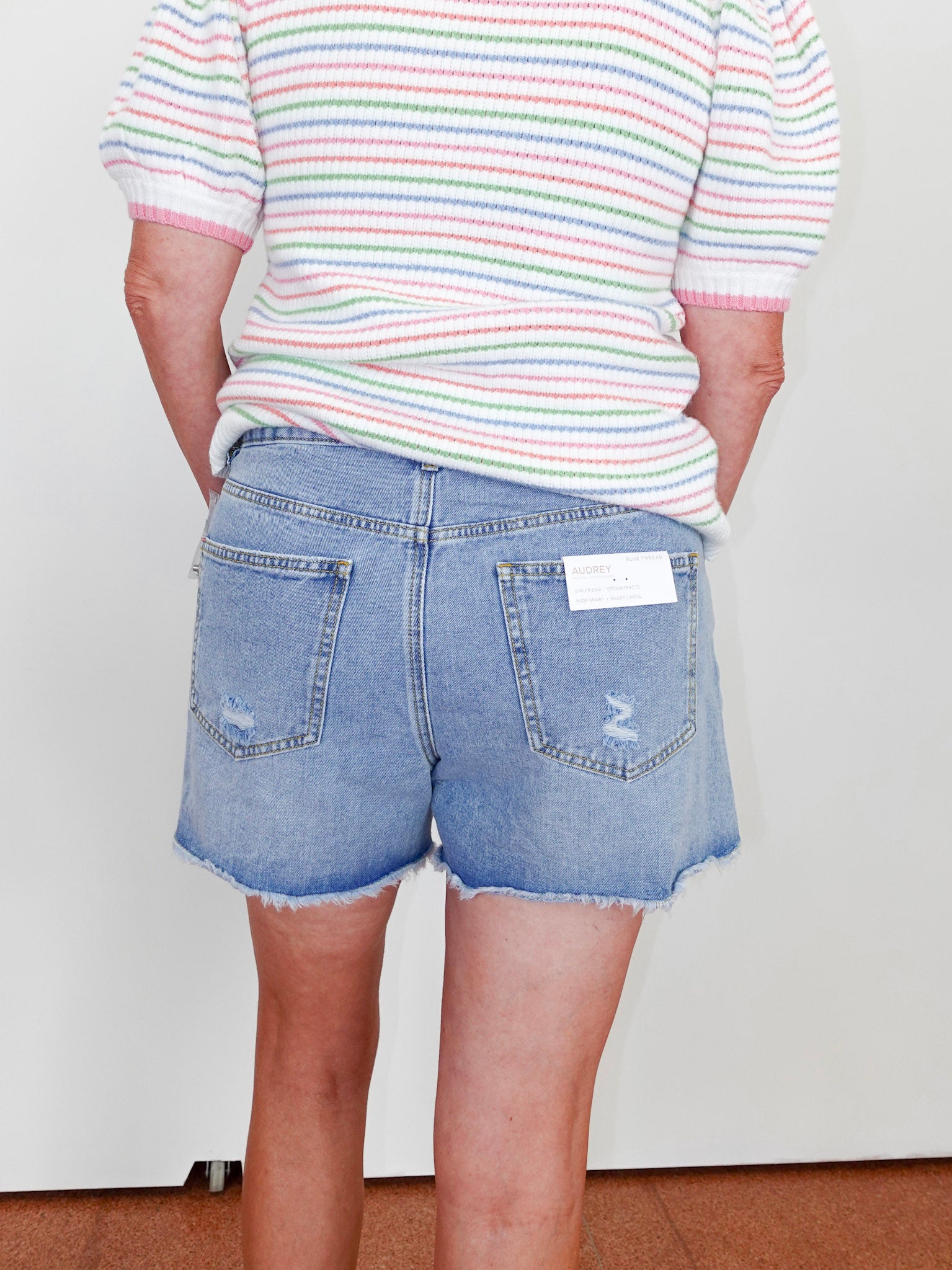 Person wearing a striped shirt and denim shorts with a white background