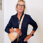 Woman wearing a denim jumpsuit with a beige bag against a white wall