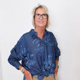 Woman wearing a blue floral blouse and beige pants against a white background