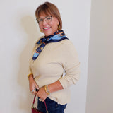 woman wearing a tan waffle knit top holding a burgundy hardback against a white background. 