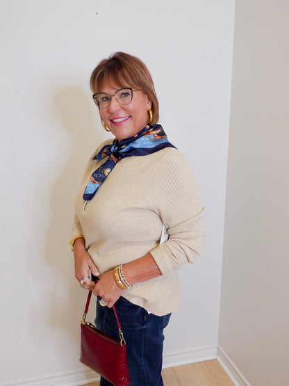woman wearing a tan waffle knit top holding a burgundy hardback against a white background. 