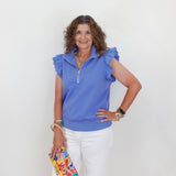 Woman wearing a blue top and white pants, holding a colorful clutch against a white background