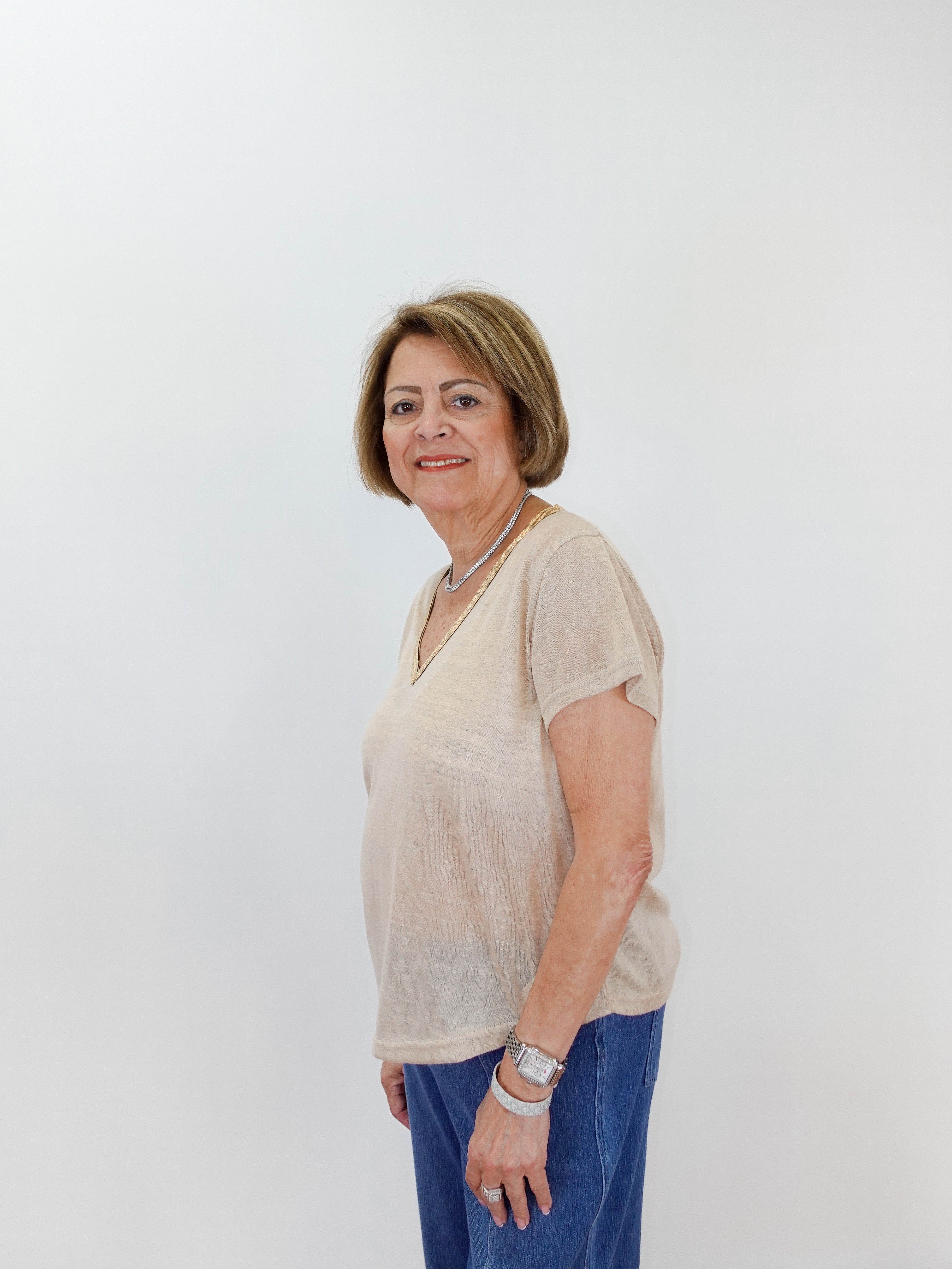 Woman wearing a beige top and blue pants against a white background