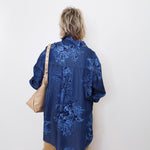 Person wearing a blue embroidered shirt against a white wall