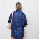 Person wearing a blue embroidered shirt against a white wall