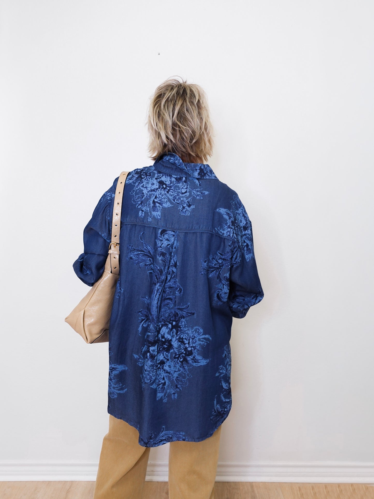Person wearing a blue embroidered shirt against a white wall
