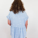 Person wearing a light blue blouse with star patterns on a plain background