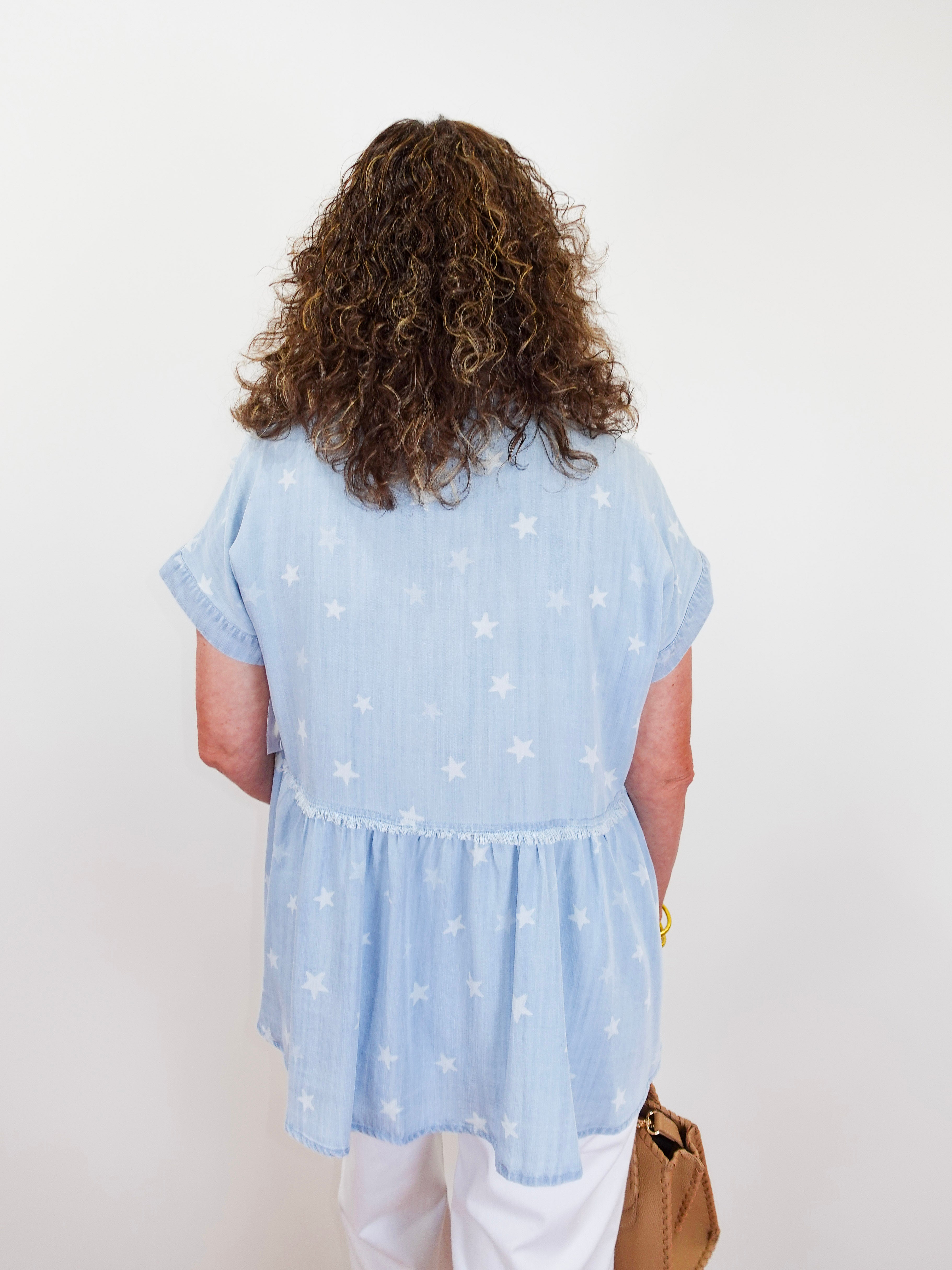 Person wearing a light blue blouse with star patterns on a plain background