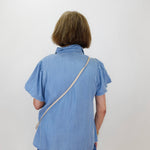 Person wearing a blue shirt with a strap over their shoulder against a white background