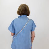 Person wearing a blue shirt with a strap over their shoulder against a white background