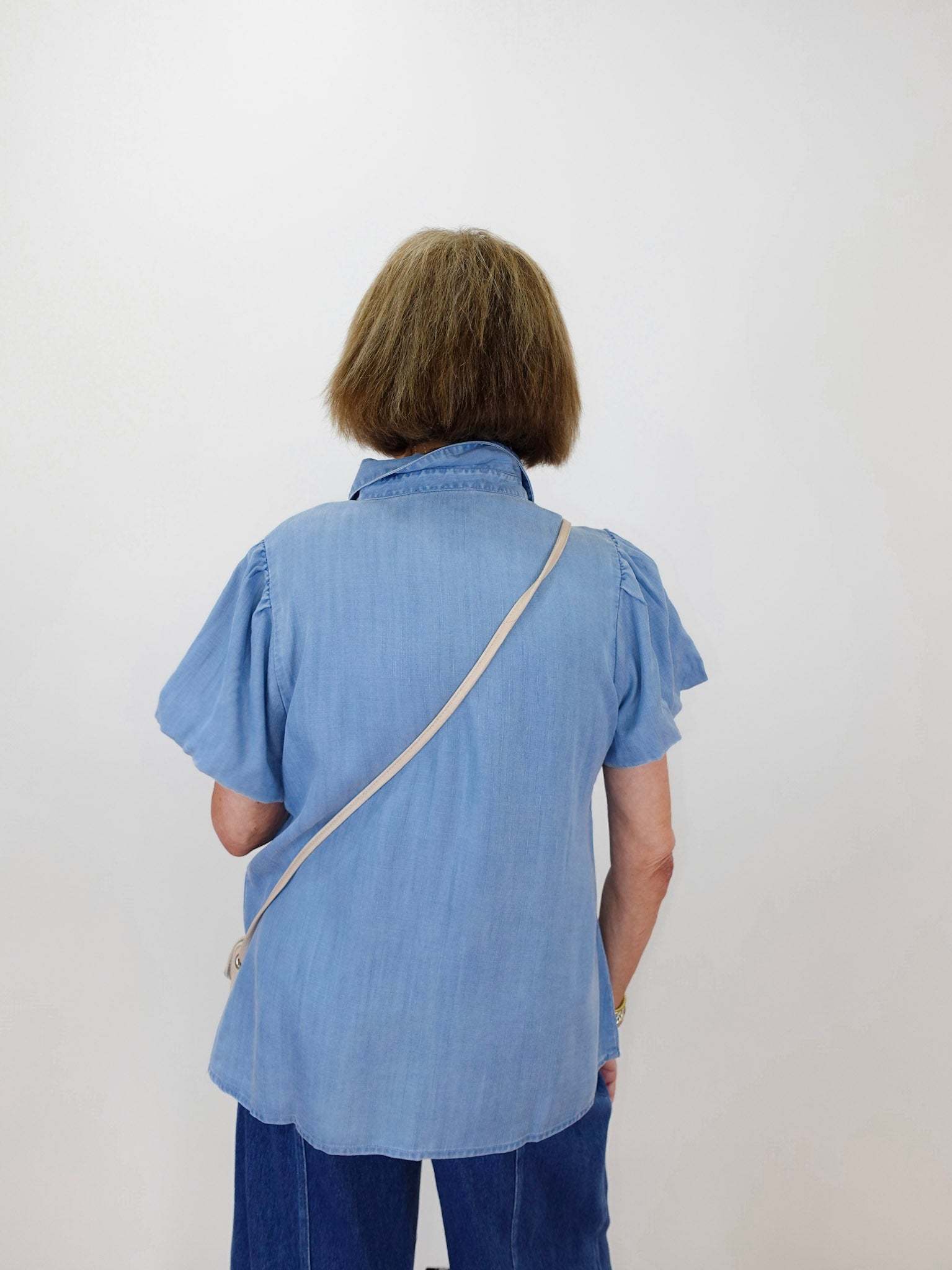 Person wearing a blue shirt with a strap over their shoulder against a white background