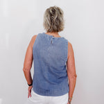 Person wearing a blue denim sleeveless top against a white background