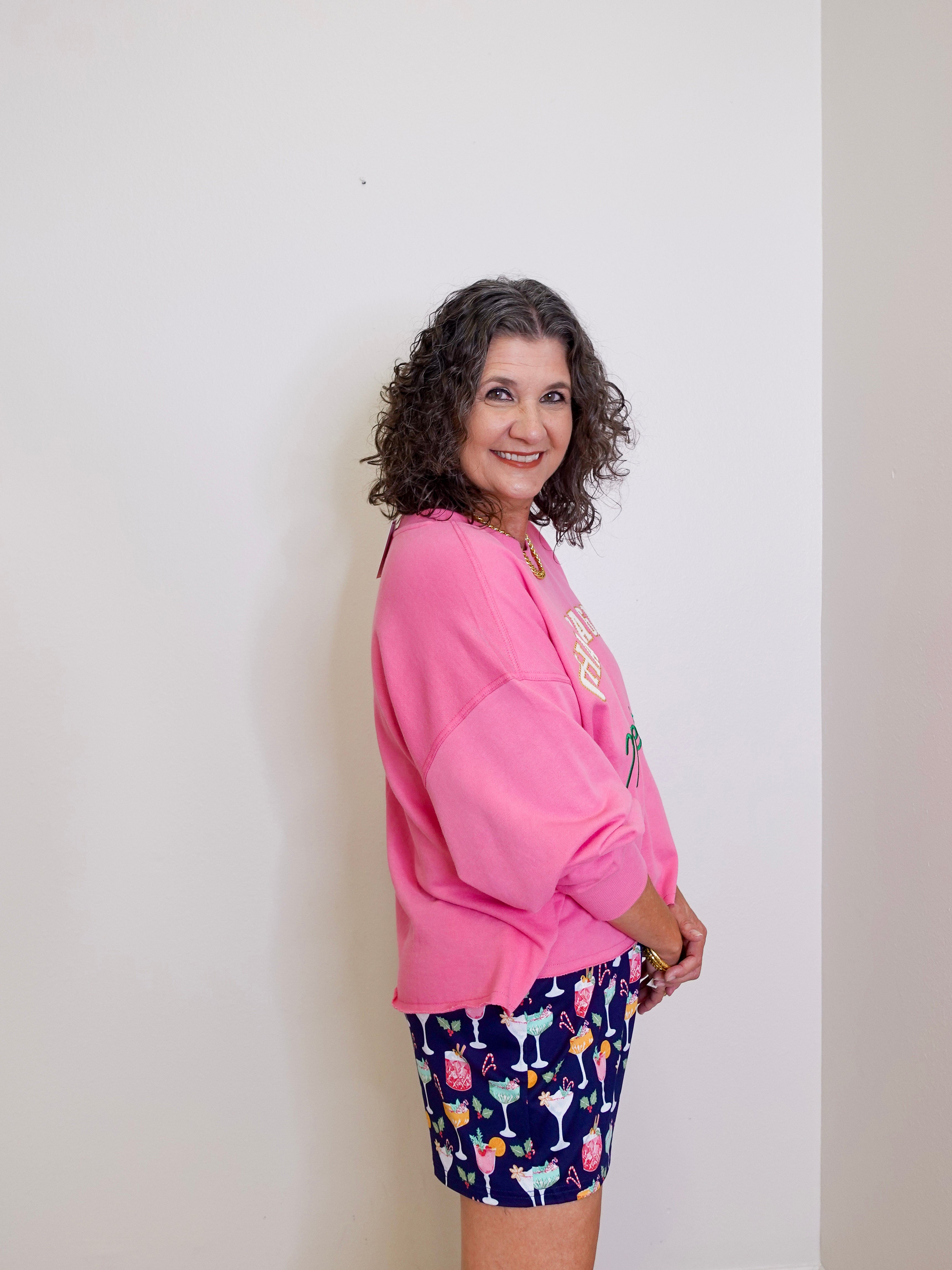 Woman wearing a pink sweatshirt and patterned shorts against a plain background