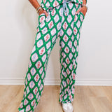 Person wearing a green and pink patterned outfit with white shoes on a light wooden floor.