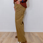Person wearing brown pants and leopard print shoes against a white wall.