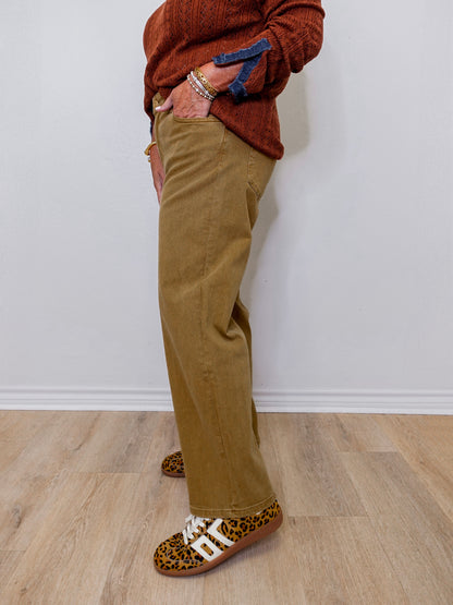Person wearing brown pants and leopard print shoes against a white wall.