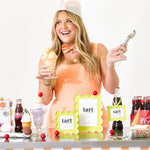 Woman in a dessert-themed costume holding ice cream and a spoon, with a table full of candy and drinks.