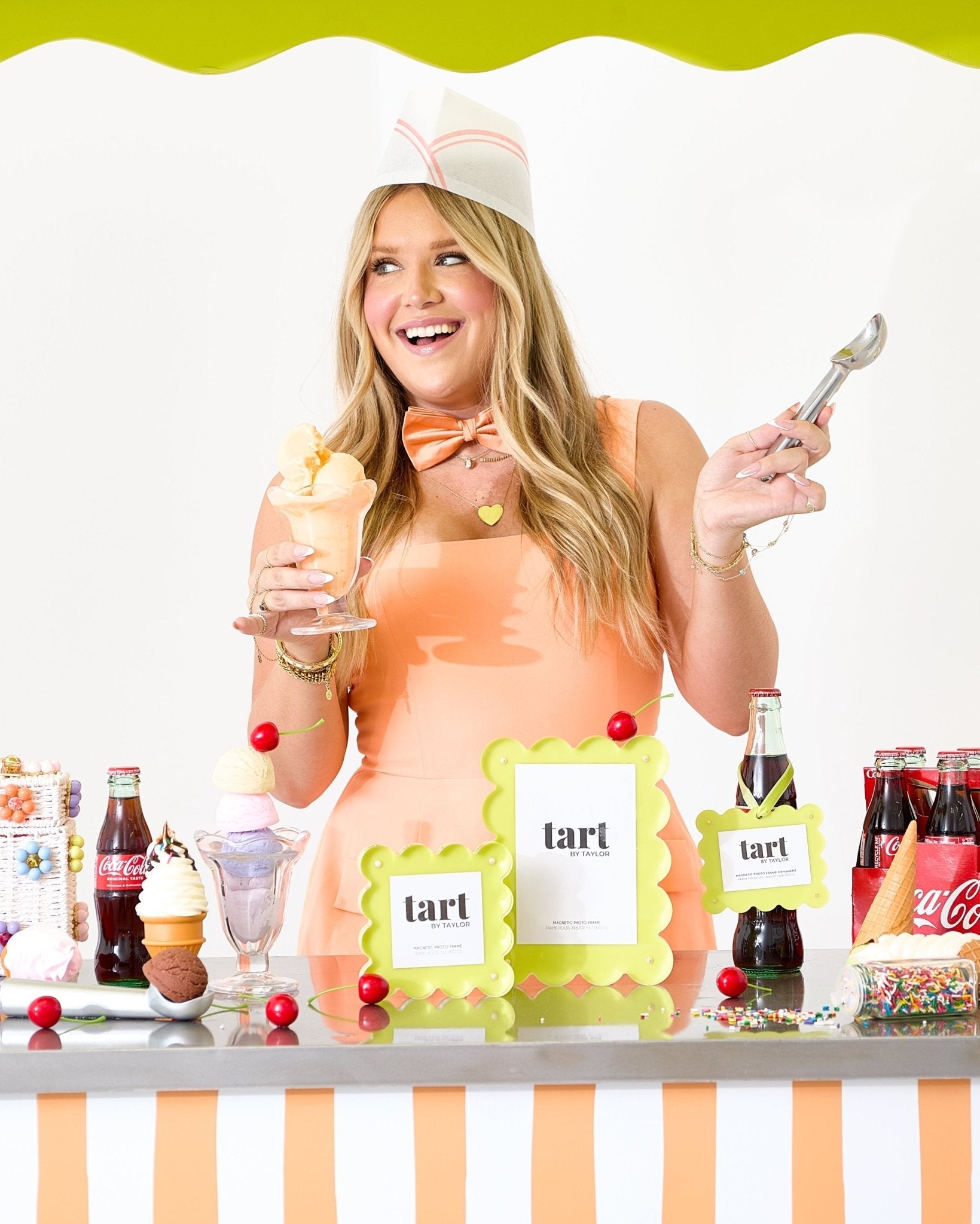 Woman in a dessert-themed costume holding ice cream and a spoon, with a table full of candy and drinks.