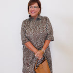 Woman wearing a leopard print dress holding a brown handbag against a white background