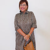 Woman wearing a leopard print dress holding a brown handbag against a white background