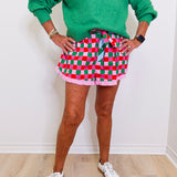 Person wearing a green sweater with 'JOY' print, red and green checkered skirt, and white sneakers on a light wooden floor.