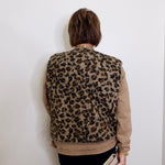 Person wearing a leopard print vest against a white wall