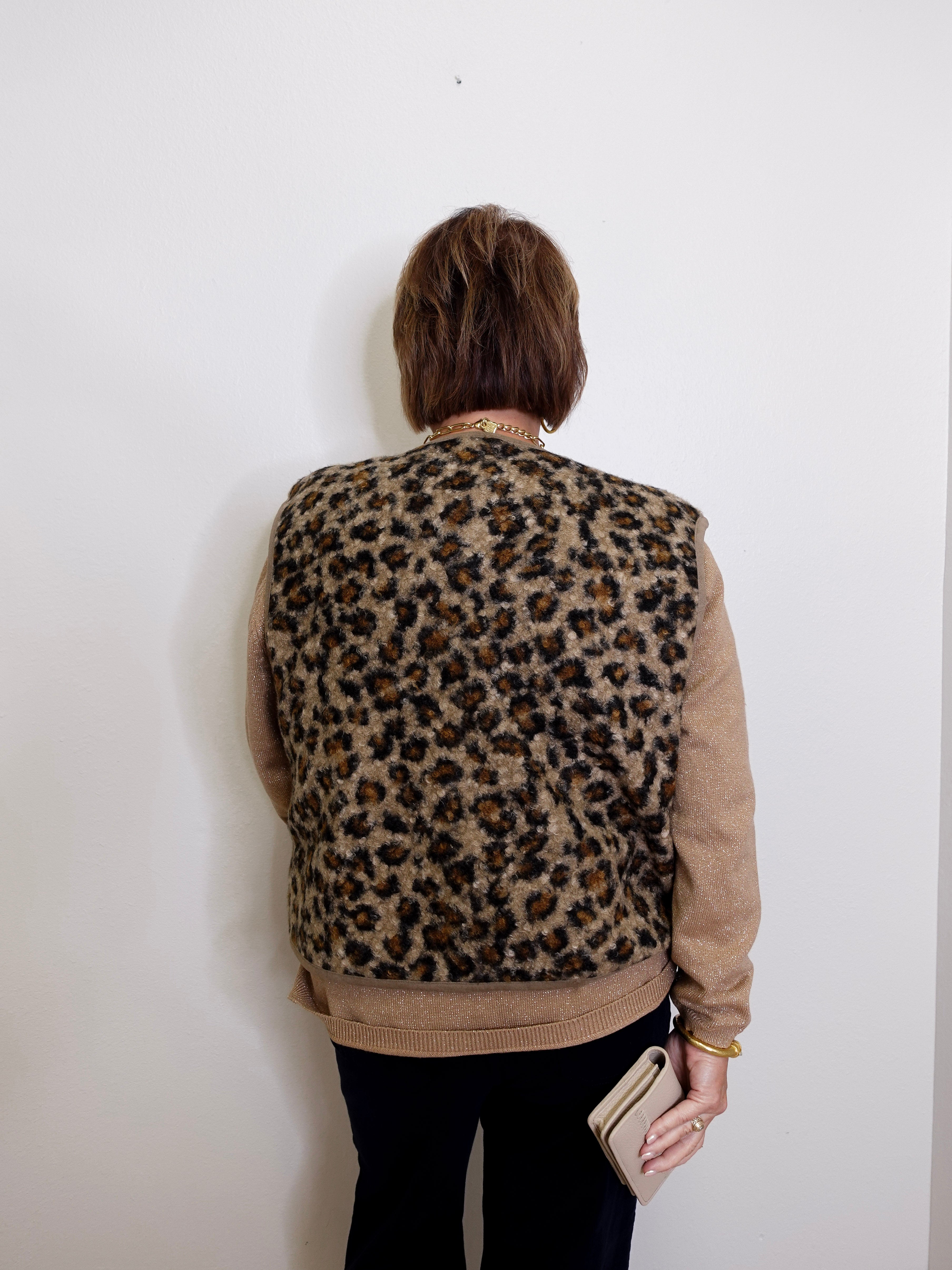 Person wearing a leopard print vest against a white wall
