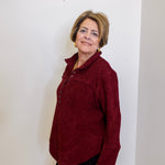 Woman wearing a casual wine color chenille henley top with grommet accents in front a white background 
