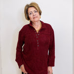 Woman wearing a chenille Henley top with grommet details in front a white background. 
