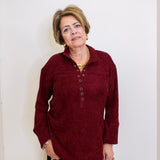 Woman wearing a chenille Henley top with grommet details in front a white background. 
