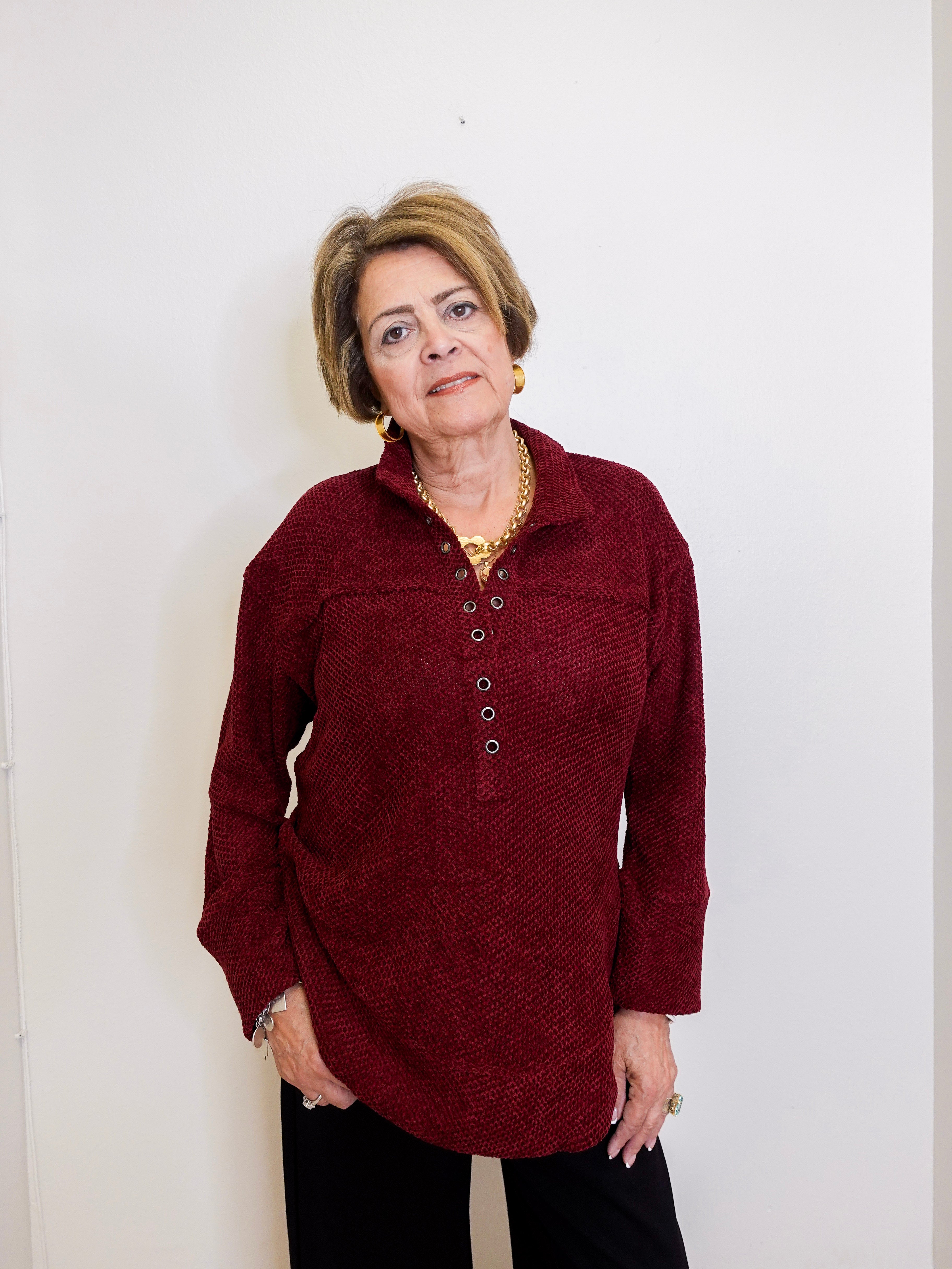 Woman wearing a chenille Henley top with grommet details in front a white background. 
