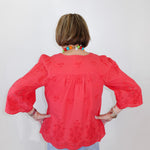 Person wearing a coral blouse with floral patterns against a white background