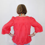 Person wearing a coral blouse with floral patterns against a white background