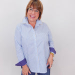 Woman wearing a blue and white striped shirt with rolled-up sleeves against a plain background