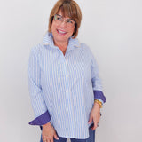 Woman wearing a blue and white striped shirt with rolled-up sleeves against a plain background
