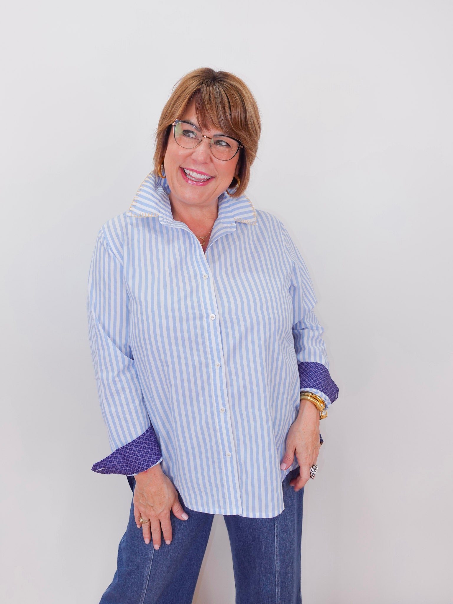 Woman wearing a blue and white striped shirt with rolled-up sleeves against a plain background